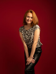 Fototapeta premium a modern stylish girl with golden hair in leather trousers and a spotted blouse on a red background