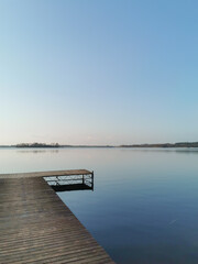 Obraz premium Lake view with a wooden pier in the lower left corner. Blue sky and water at the dusk. Calm scene of nature and nobody.