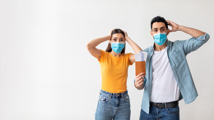 Cancelled flight. Shocked couple in medical face masks holding travel tickets, light background, free space