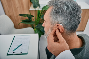 Audiologist fits a hearing aid on deafness mature man ear while visit a hearing clinic. Hearing...
