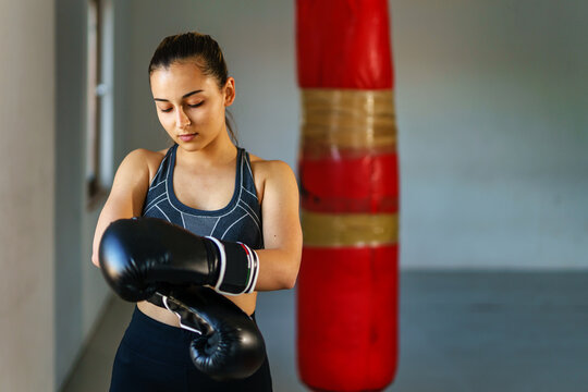 Front view portrait of young caucasian woman or teenage girl wearing boxing gloves - female boxer adjusting gloves waist up copy space