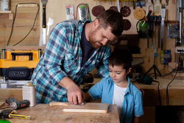 Father carpenter and son boy work in the workshop. Master dad teaches his son carpentry. Continuity of generations. Small business.