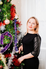 a blonde woman in a black dress by the Christmas tree. a single unmarried woman. dating site. happy Christmas holidays. cosmetology and medicine for women.