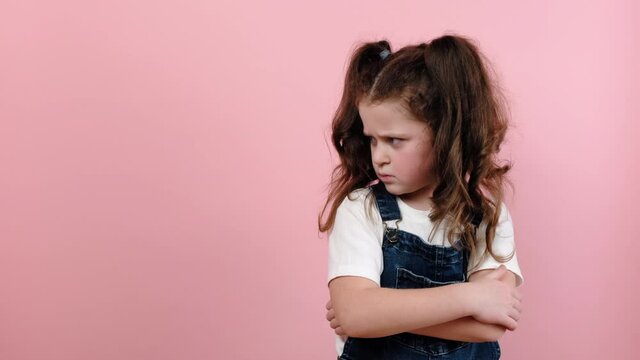 Naughty child concept. Disobedience problem. Discipline punishment. Portrait of angry offended little girl kid with crossed arms, posing isolated over pink color background in studio with copy space