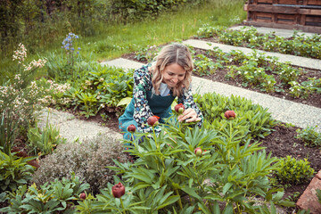 pretty blonde gardener working in garden with flowers and wearing green work apron