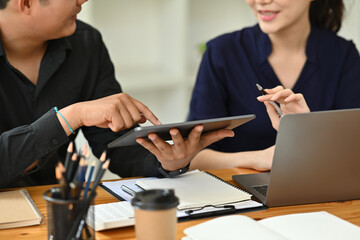 Cropped image of businesspeople working together at the wooden table surrounded by a computer laptop, paperwork, calculator and various office equipment.