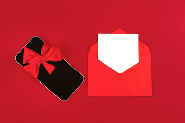 Black mobile phone with red ribbon bow and blank white paper note inside of envelope against red...