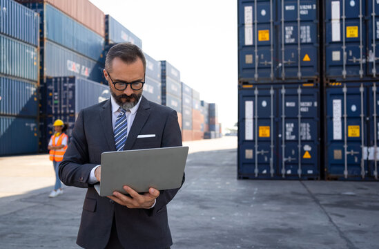 The warehouse manager or business man are using laptops view oranalytics warehouse information. He used technology to help with warehouse management at shipyards in transportation logistic concept
