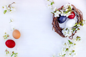 nest with Easter eggs and branches of spring flowering cherries on a white wooden background. Rye eggs painted with natural dyes.