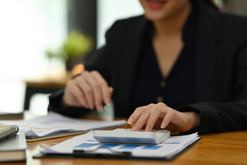 Cropped image of a young accountant woman calculates the business growth at the wooden table surrounded by a computer laptop and business paperwork.