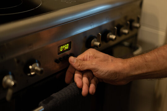 Looking down at man turning on electric oven with control knobs at home
