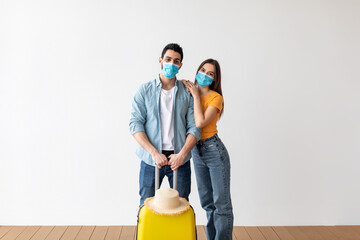 New travel rules. Loving couple in face masks, standing with luggage ready for vacation trip during coronavirus pandemic