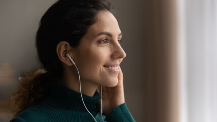 Close up head shot young attractive woman listening favorite popular music in wired earphones,...