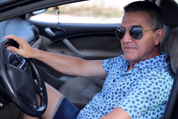 a 60 year old man who takes care of himself, is healthy and attractive and poses in his car with 
his blue shirt
