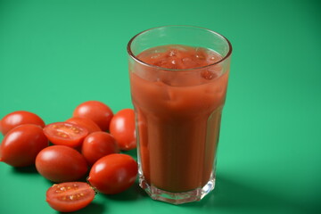 Full glass of fresh tomato juice with cherry tomatoes around . Very tasty and healthy tomato juice with ice cubes