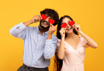 Lovers blinded by their big love. Young indian couple in love holding red heart-shaped cards over...