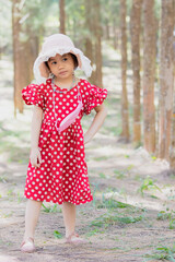 Asian girl wear red dot dress with beautiful hat standing in pine forest.