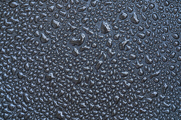 Drops, drips, blobs, beads, dribbles of water on the black teflon surface. Monochrome black and white macro or closeup background or texture