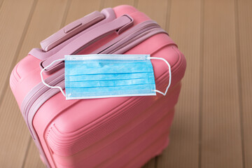 Travel concept under the conditions and restrictions due to Coronavirus 2019-nCov. Pink suitcase with medical face mask