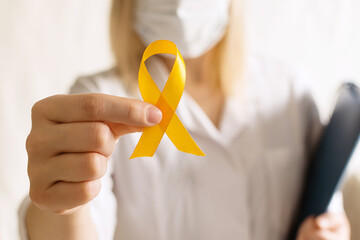 International Childhood Cancer Day. Female doctor in coat holds yellow ribbon on white background....