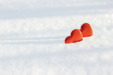 two red hearts lie on the snow in the sunlight, romantic minimalism