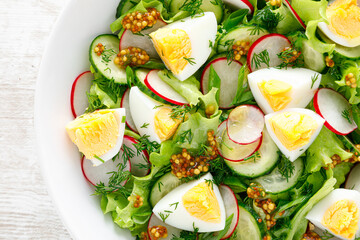 Easter fresh vegetable salad with boiled egg, radish and cucumber, dressing with dijon mustard and lemon on white wooden table. Top view