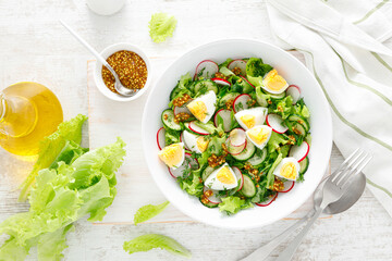 Easter fresh vegetable salad with boiled egg, radish and cucumber, dressing with dijon mustard and lemon on white wooden table. Top view
