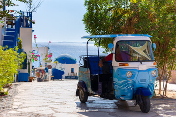 Traditional tuk-tuk moto taxi is waiting for passengers on empty road to sea at resort. Popular...