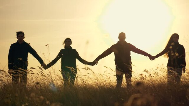 Family of four silhouette at sunset. Group of happy business team joins hands for business success, teamwork. Success hand, team unity concept. Family silhouette together hand in hand