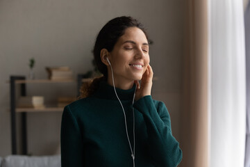 Happy inspired young woman wearing wired earphones, listening favorite popular music or...