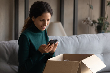 Beautiful millennial gen hispanic latin female client feeling satisfied with received order from internet store, leaving review or typing recommendation in cellphone application, shopping concept.