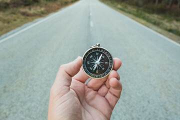 a hand holding a compass on a highway. Concept of orientation and leadership