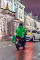 Fototapeta na wymiar Food delivery boy on scooter at night with isothermal food case.