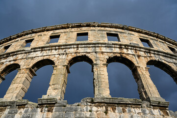 Obraz premium Pula, Istria, Croatia: Ancient amphitheater from Roman era in city centre. Monument against dark and dramatic clouds. Cultural heritage and famous landmark. Pulska Arena