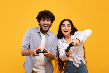 Free time entertainment concept. Joyful indian couple playing video games together, holding and...