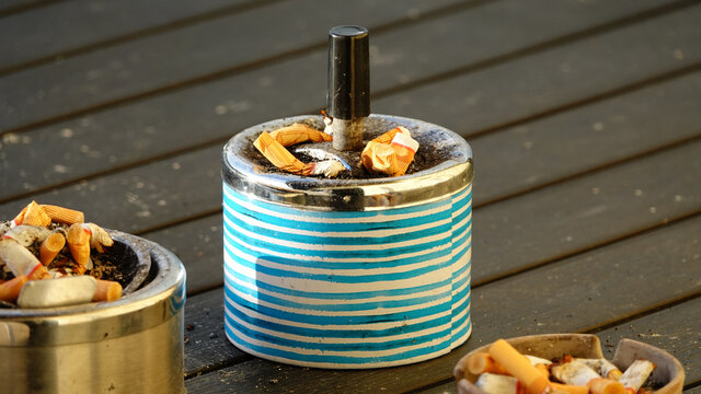 Drei mit Zigarettenkippen gef&uuml;llte Aschenbecher auf einem Holztisch