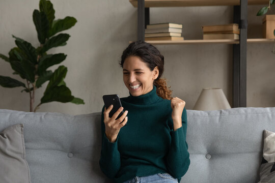Emotional happy laughing millennial latin woman looking at smartphone screen, feeling excited of getting win news, celebrating online achievement or internet lottery gambling auction victory.