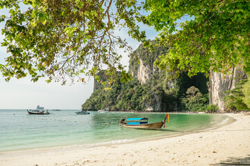 Tropical beach with limestone cliffs covered with greenery and boats in the sea