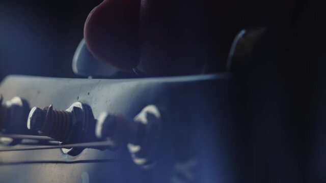 The musician tunes the guitar by turning the tuning pegs. Closeup of the left hand. Macro shooting. Depth of field