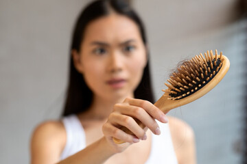 Worried millennial asian woman holding hairbrush, closeup