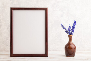 Wooden frame with blue muscari hyacinth flowers in ceramic vase on gray concrete background. side view, copy space, mockup.