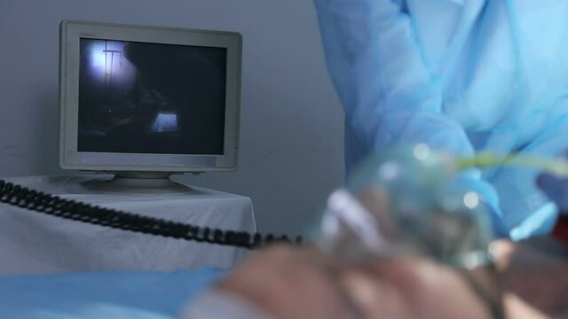 Doctor in operating room trying to help on intensive care patient, use defibrillator electrical device to shock heart. Looks at the monitor with vital data