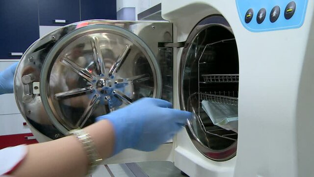 Laboratory workers packing up medical instruments and putting into steam autoclave sterilization machine. Dental clinic. Disinfection process. Stomatology 