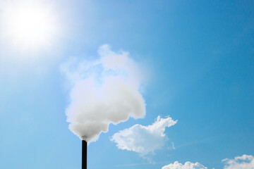 Thick white smoke coming out of the chimney against blue sky with sun and clouds. Background for air pollution. Concept idea of white smoke from the chimney indicates that the Pope has been elected