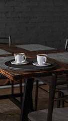 two mugs of coffee stands on a tray in a restaurant.  dark colors, loft style interior.  no people