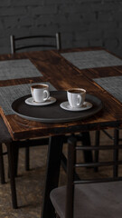two mugs of coffee stands on a tray in a restaurant.  dark colors, loft style interior.  no people