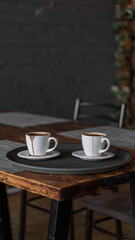 two mugs of coffee stands on a tray in a restaurant.  dark colors, loft style interior.  no people