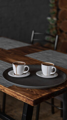 two mugs of coffee stands on a tray in a restaurant.  dark colors, loft style interior.  no people