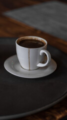 a mug of coffee stands on a tray in a restaurant.  dark colors, loft style interior.  no people