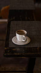 a mug of coffee stands on a tray in a restaurant.  dark colors, loft style interior.  no people